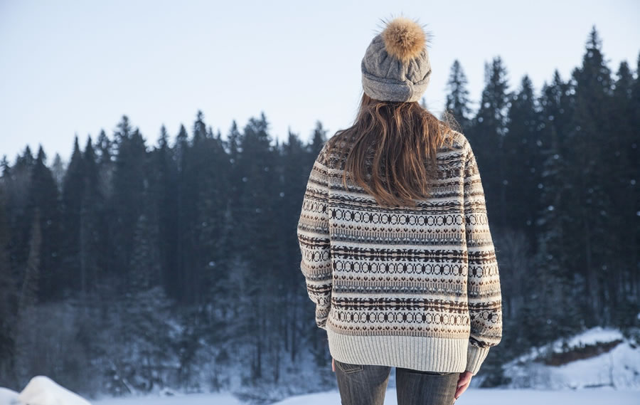 Woman with sweater and knit hat looking at snowy trees