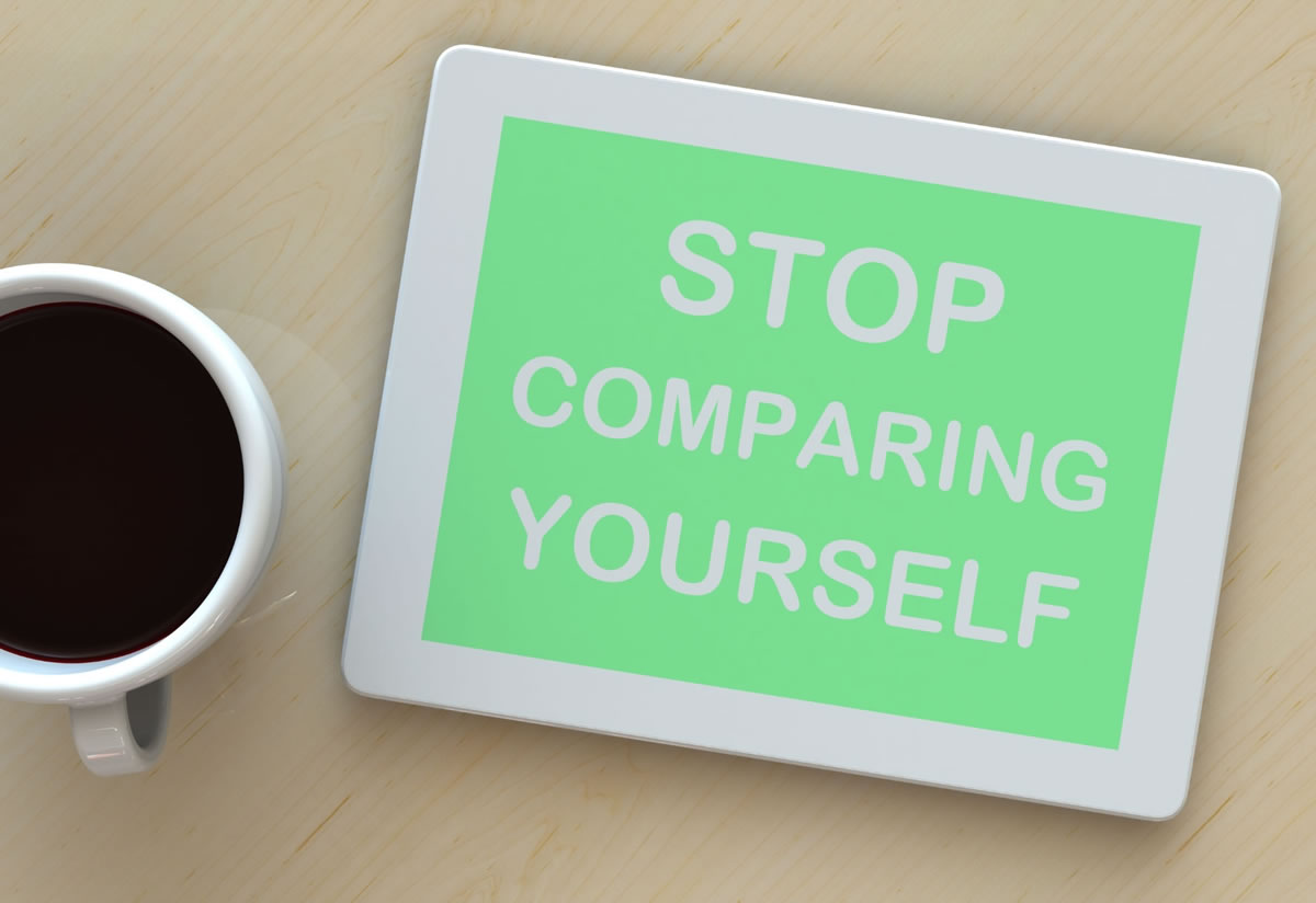 A sign of 'stop comparing yourself' on a table next to a cup of coffee