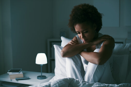 a woman sitting in bed with her headphones on - Depressed woman in her bed