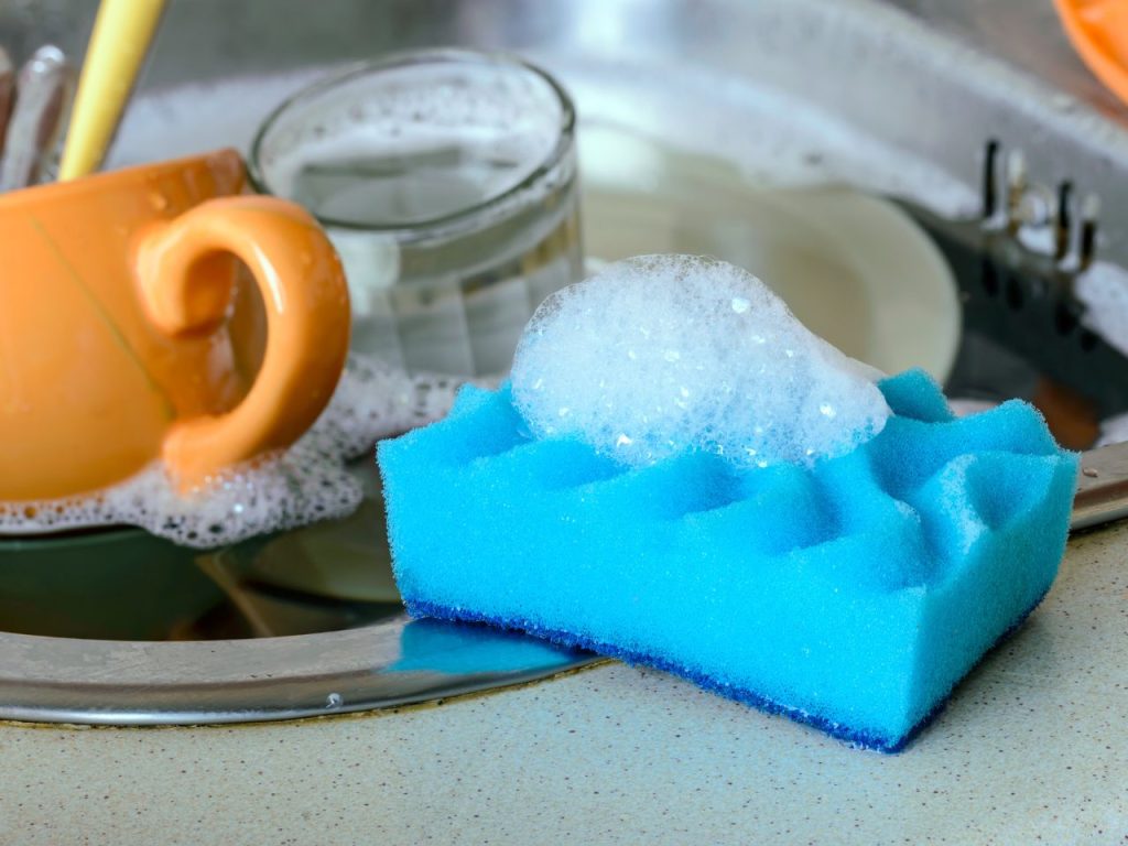 A dish sponge on the sink next to a pile of dirty dishes