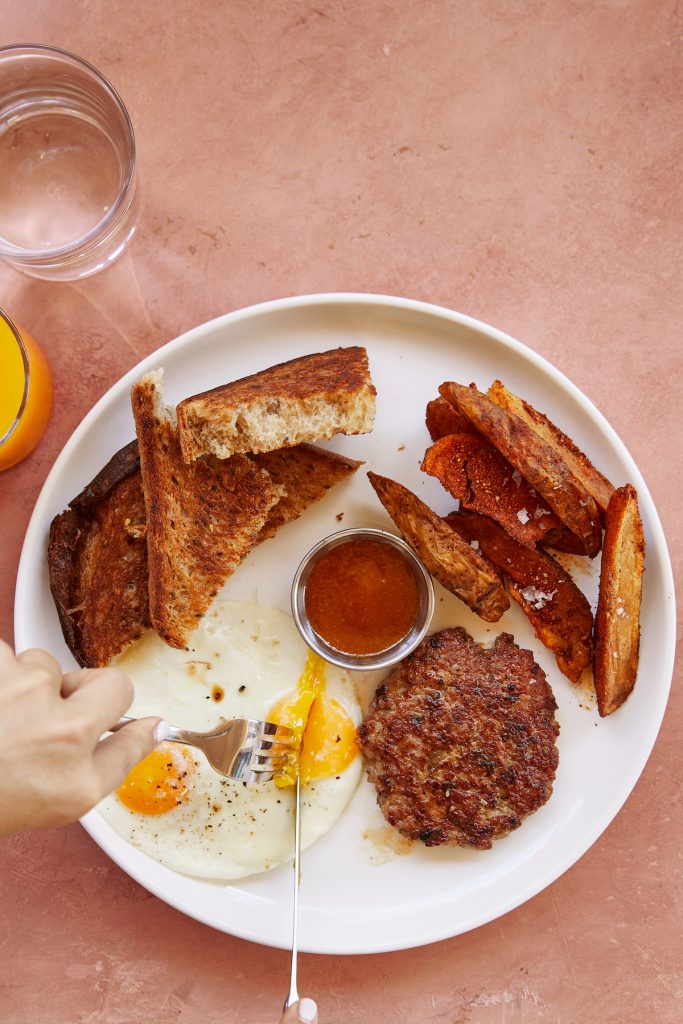 Frühstück bei Paperboy in Austin.  Weißer Teller mit Toast, Wurst, Eiern, Kartoffeln und Ketchup.