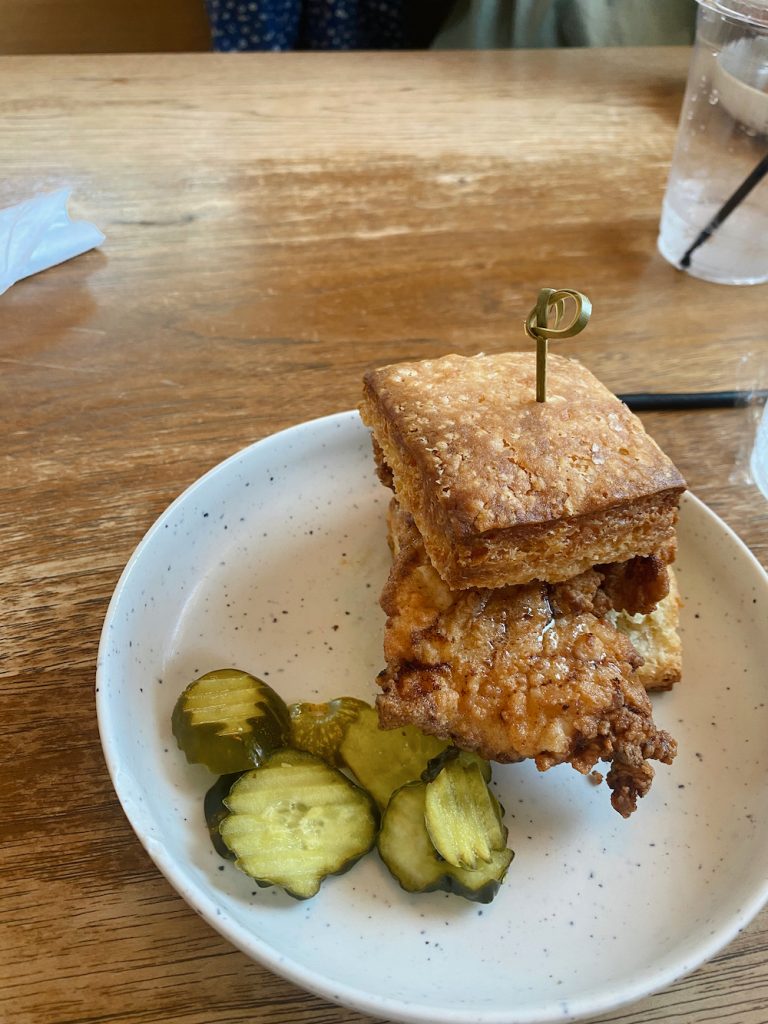 Gebratenes Hühnerkeks-Sandwich und Gurkenchips auf gesprenkeltem weißem Teller bei Better Half Coffee & Cocktails in Austin.
