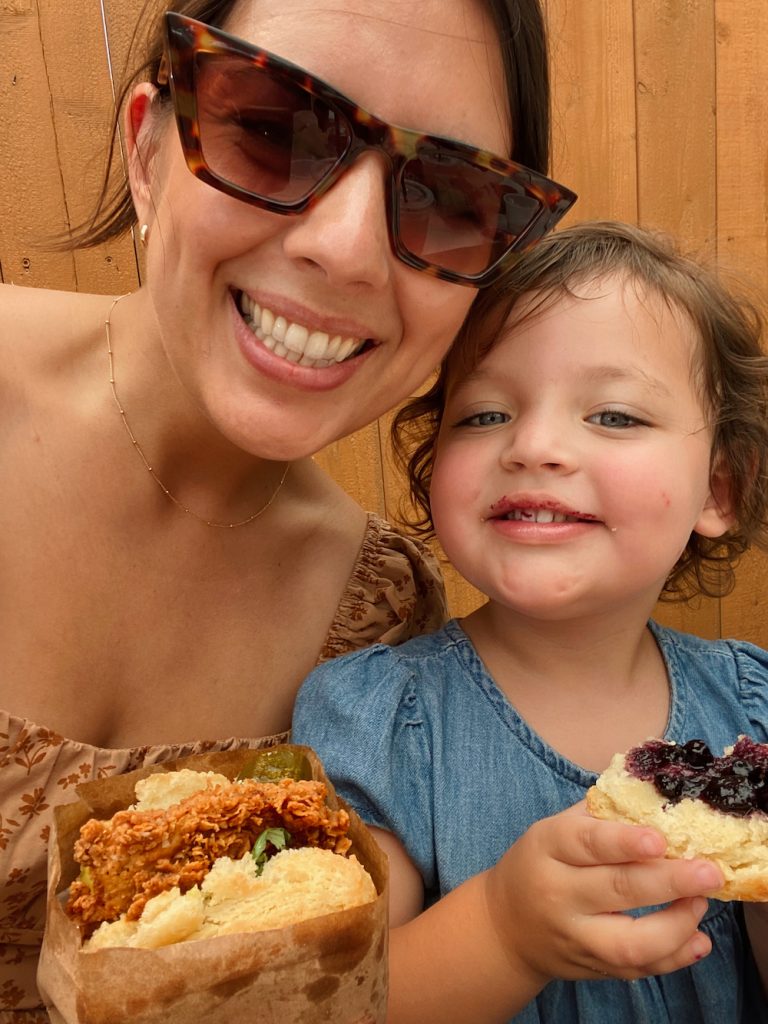 Mutter und Tochter lächelnd mit gebratenem Hähnchen-Sandwich bei Bird Bird Biscuit in Austin.