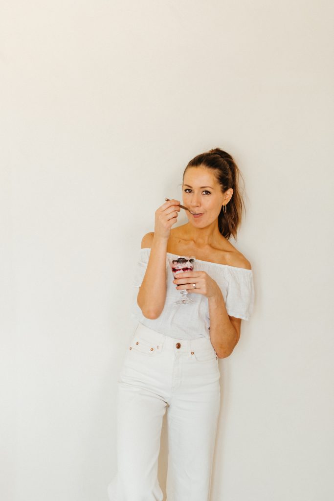 Brunettefrau, die weißes Hemd und Jeans trägt und Parfait-Dessert isst.