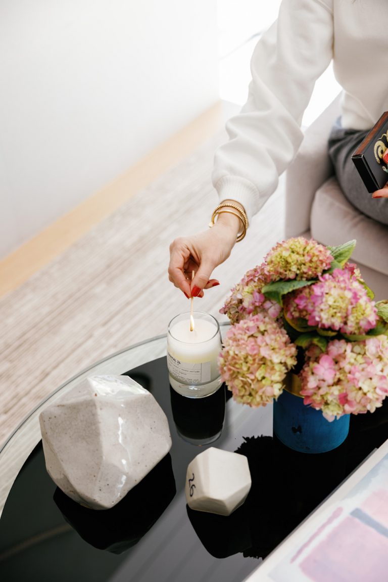 Frau mit roten Nägeln, die weiße Kerze auf schwarzem Tisch mit rosa Hortensien anzündet. 